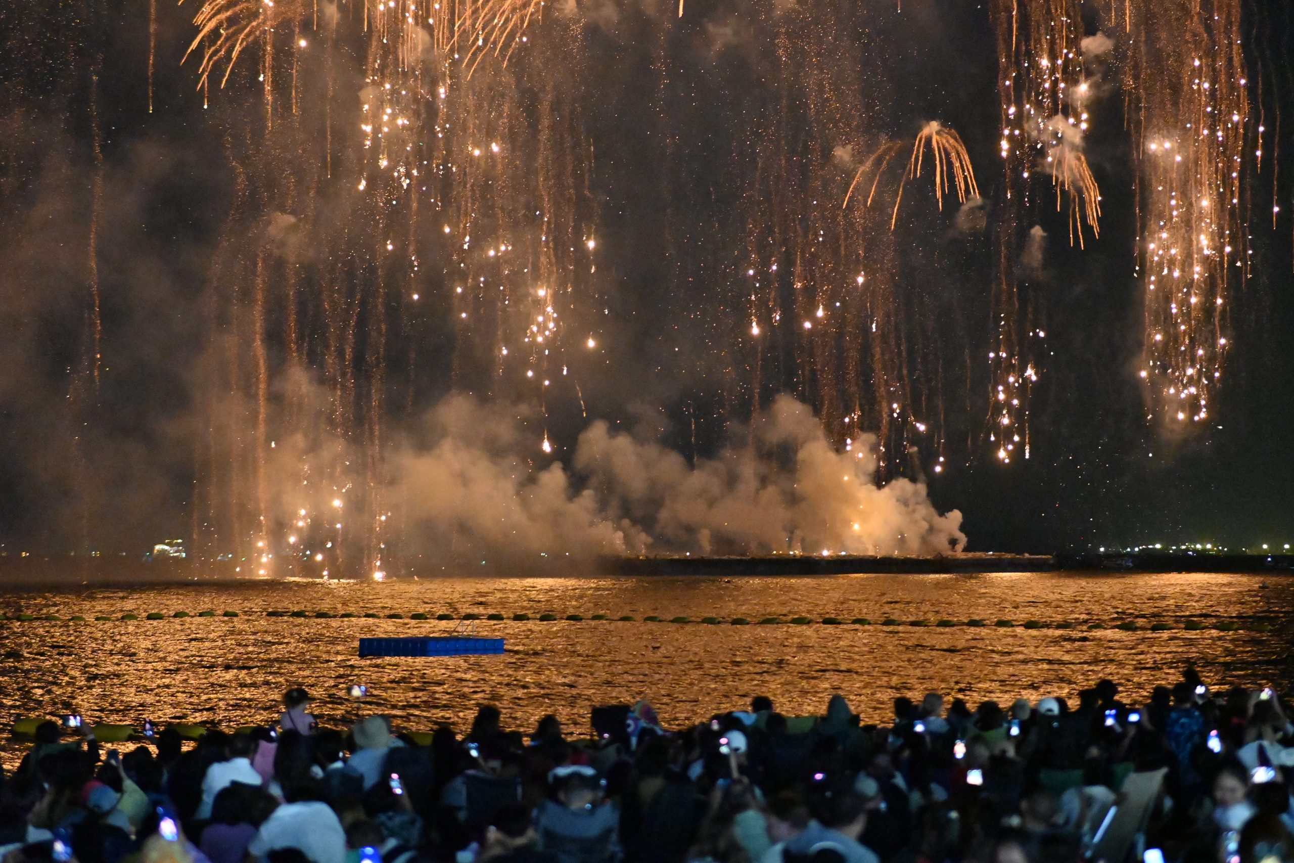 Golden New Year fireworks cascading over water with reflections shimmering on the surface