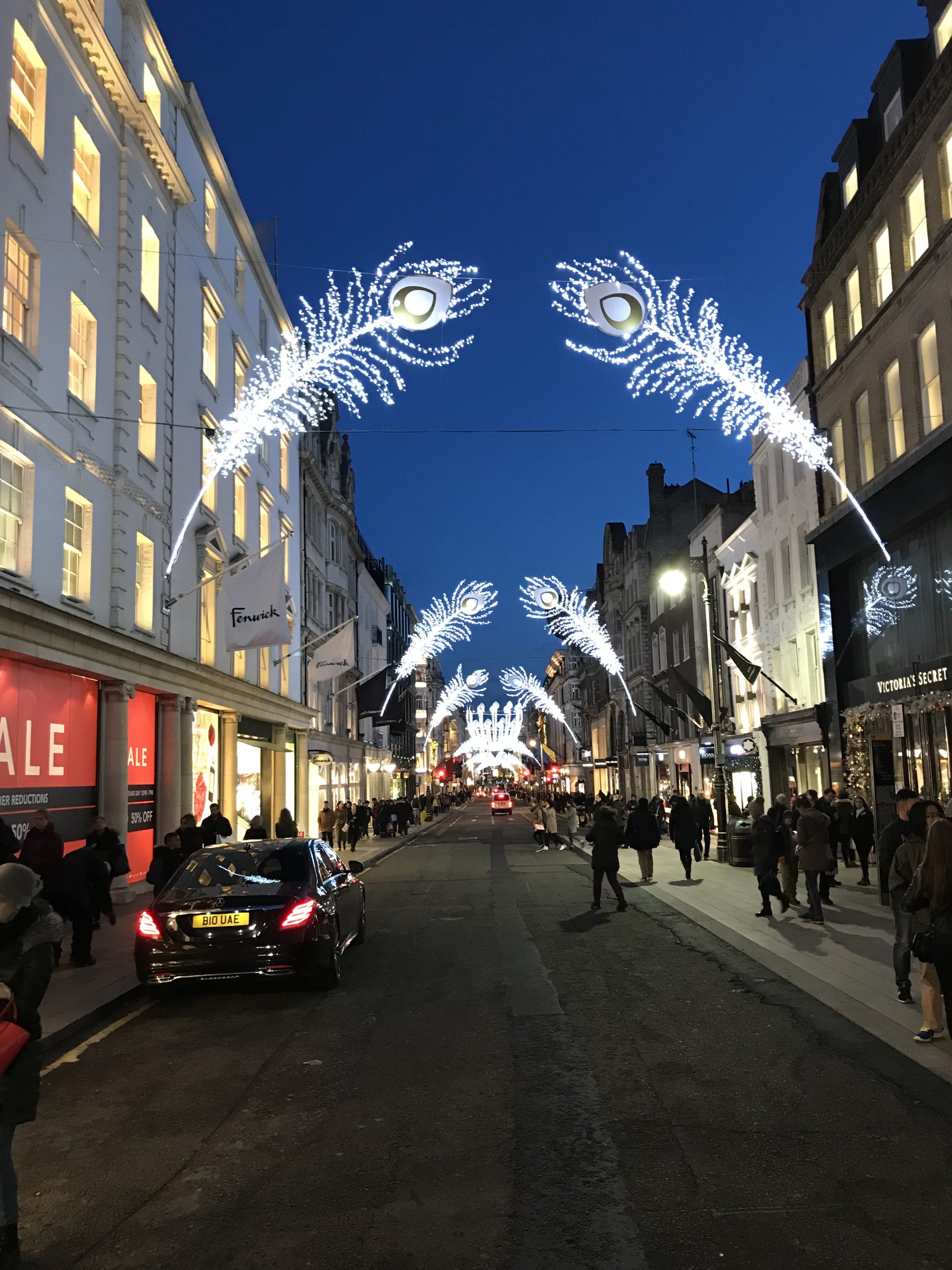 Illuminated angel light decorations hanging above a busy shopping street at night