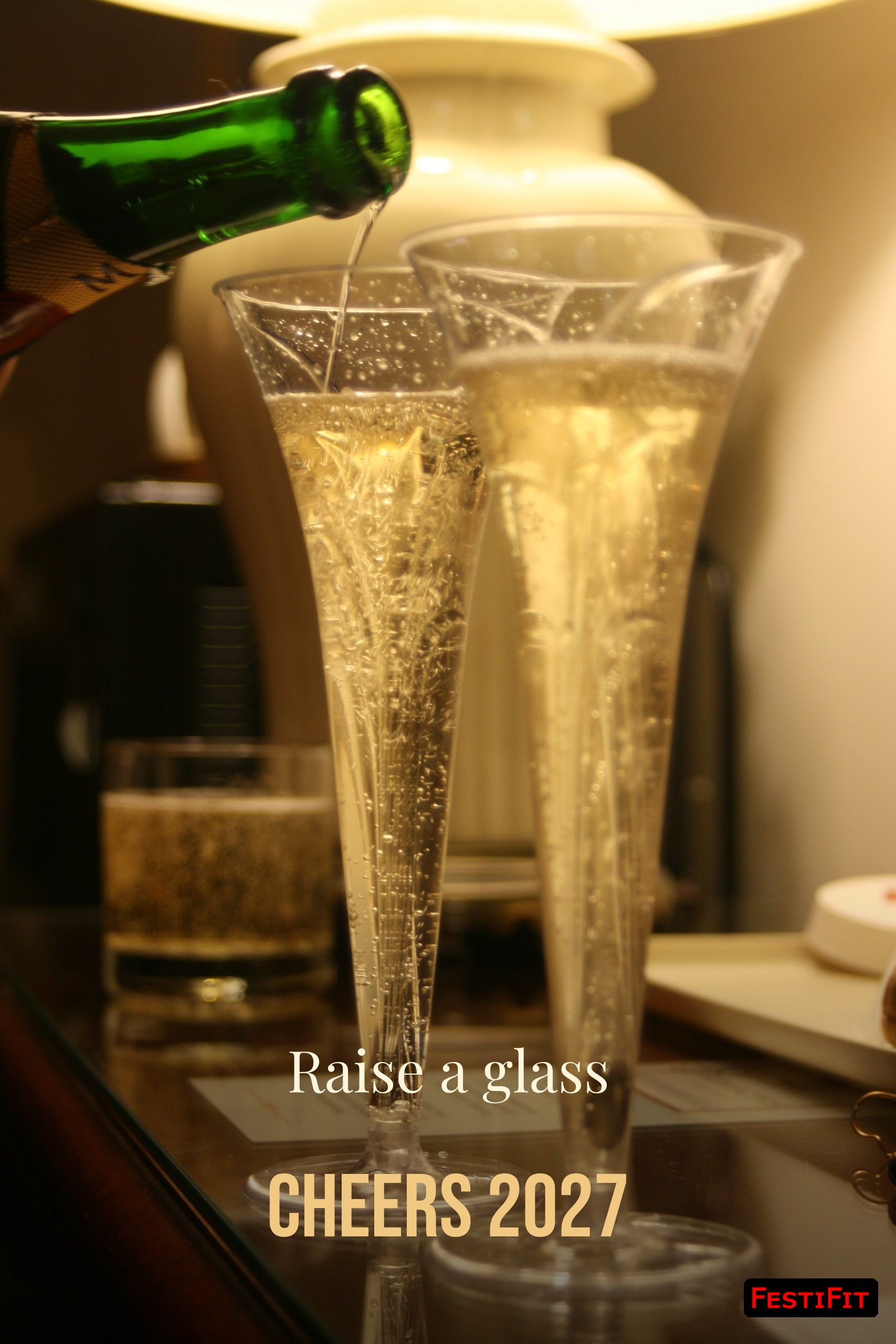Raise a glass Cheers 2027 over champagne pouring into glasses vertical, FestiFit watermark